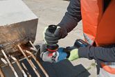 A person wearing safety equipment cuts metal rebar from concrete using an angle grinder.