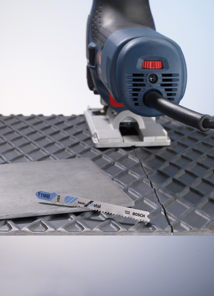 Jigsaw cutting a metal sheet on a textured surface.