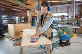 Person wearing safety equipment sanding a wooden tabletop with a random orbit sander.