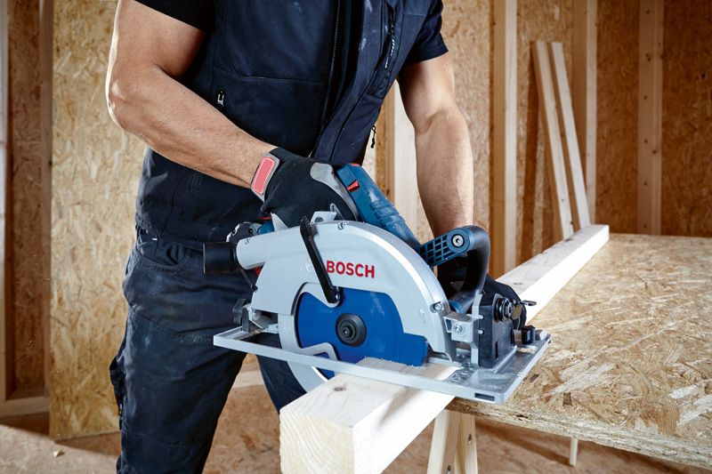 A person wearing safety equipment uses a circular saw to cut a wooden board.