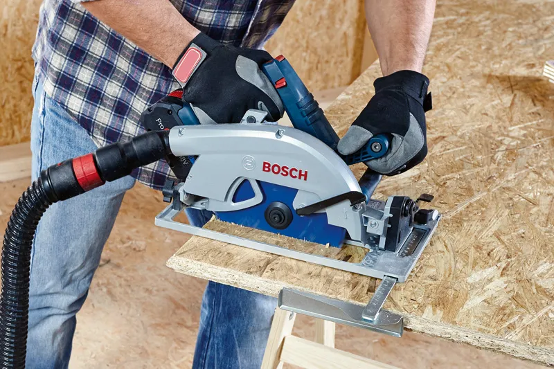 Person wearing safety equipment cuts oriented strand board with a circular saw.