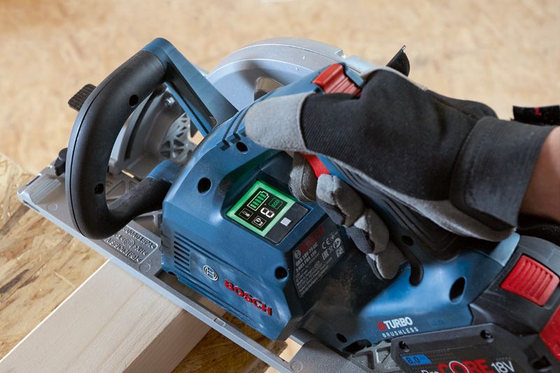 A person wearing safety equipment operates a cordless circular saw on a wooden board.