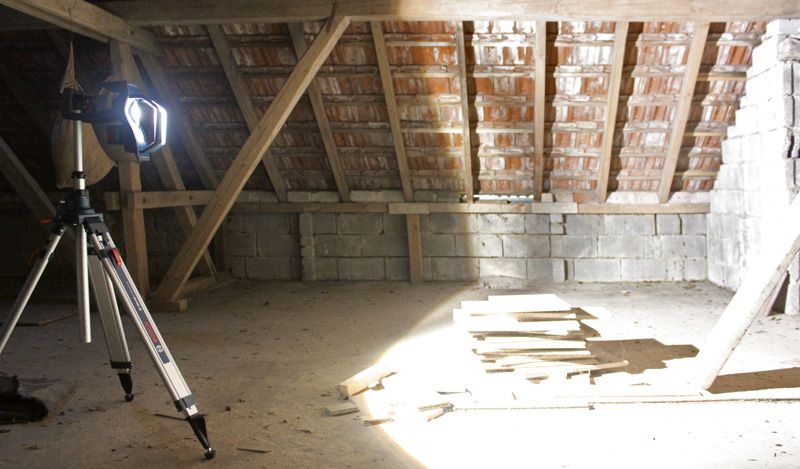 GLI 18V-10000 C Jobsite light on a tripod brightly illuminates stacked boards in an unfinished attic.