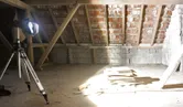 Jobsite light on a tripod brightly illuminates stacked boards in an unfinished attic.