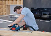 A person wearing safety equipment cuts wood using a circular saw with dust extraction.