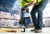 A person wearing safety equipment uses a cordless rotary hammer to drill into concrete.