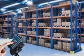A person uses a laser measure to check distances between warehouse shelves.