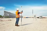 A person wearing safety equipment uses a laser leveling tool on a construction site.