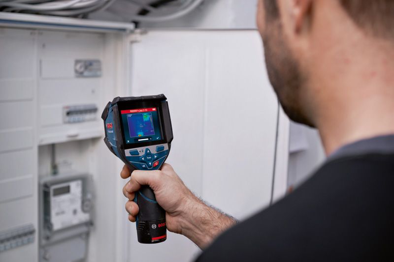 A person uses a thermo camera to inspect an electrical panel.