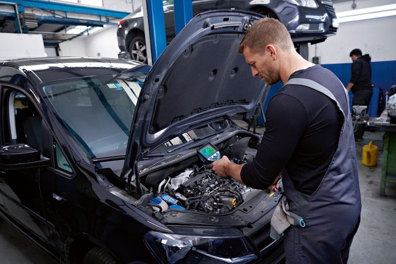 A person checks a car engine using a thermo camera in an automotive workshop.