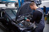 A person wearing safety equipment inspects a car engine with a thermo camera.