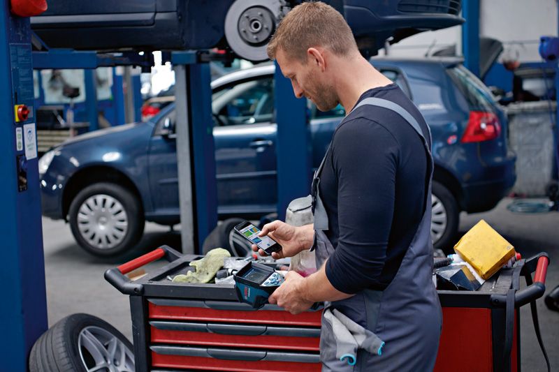 A person wearing safety equipment checks a thermo camera at a tool cart in an auto workshop.