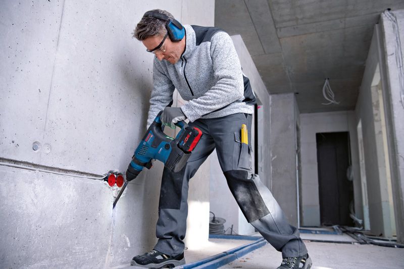 A person wearing safety equipment drills into a concrete wall in a construction area.