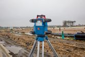 Laser leveling tool on a tripod stands at a wet construction site.