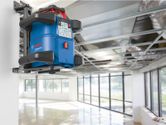 Laser leveling tool mounted on a wall in a bright, unfinished room.