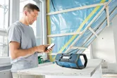 A person adjusts a phone near a blue worksite radio on a construction table.