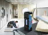 Construction radio with antenna sits on a table as a person prepares drywall panels.