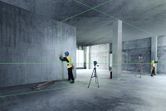 Two workers wearing safety equipment align interior walls using a laser leveling tool.