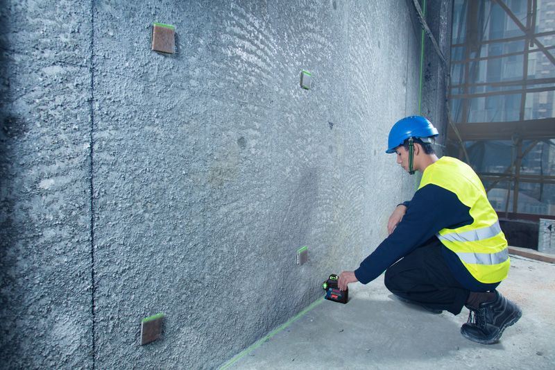 A person wearing safety equipment aligns marks on a wall using a laser leveling tool.