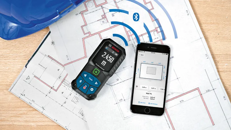 GLM 50-27 CG Laser measure and smartphone displaying measurements on construction blueprints.