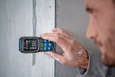 Person measures a wall with a laser measure, paint visible on their hand.