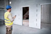 Person wearing safety equipment uses a laser measure to check doorway dimensions on a construction site.