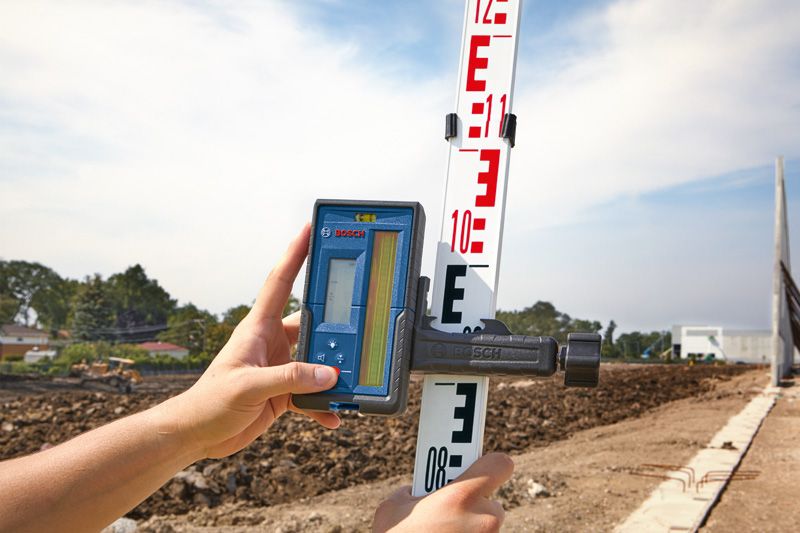 Person using a laser receiver on a leveling rod at a construction site.