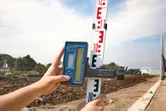 Person using a laser receiver on a leveling rod at a construction site.