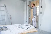 A person uses a laser measure to check wall distance at a construction site.
