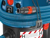 Wet and dry extractor with blue hose coiled around the unit and warning label visible.