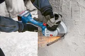 A person wearing safety equipment uses an angle grinder to cut a rebar in concrete.