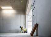 A person wearing safety equipment aligns construction points with a green laser leveling tool.
