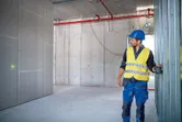 A person wearing safety equipment uses a laser leveling tool to align wall framing.