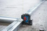 Laser leveling tool projecting green lines onto metal tracks at a construction site.