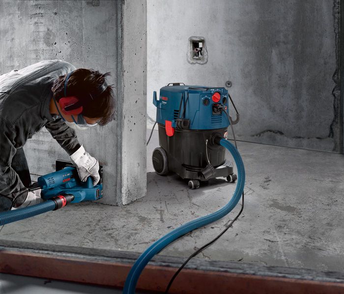 GAS 35 H AFC A person wearing safety equipment grinds concrete with a dust extractor connected by hose.