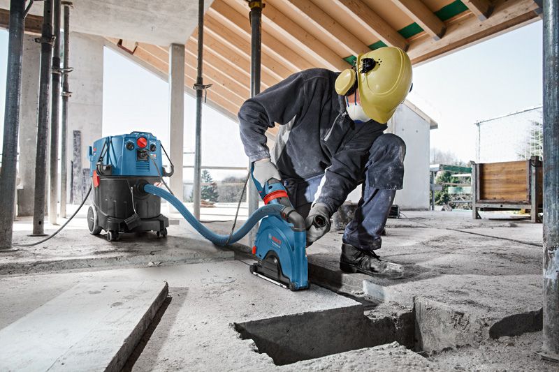 A person wearing safety equipment cuts a groove into concrete, connected to a wet/dry extractor.