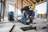 A person wearing safety equipment cuts a groove into concrete, connected to a wet/dry extractor.