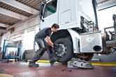Person wearing safety equipment uses an impact wrench to tighten bolts on a truck wheel.
