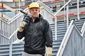 A person wearing safety equipment and a heated hoodie stands on stairs holding a power tool.
