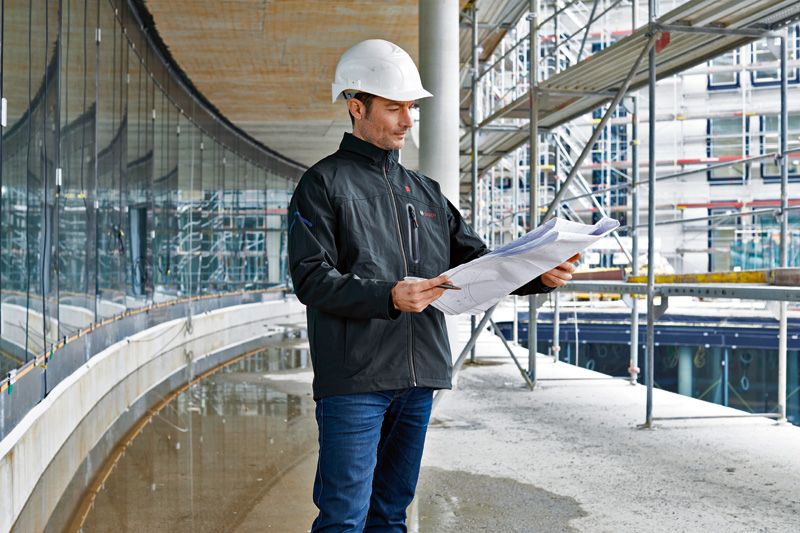 Person wearing safety equipment and heated jacket reviews blueprints at a construction site.