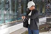 A person wearing safety equipment adjusts a heated jacket at a construction site.