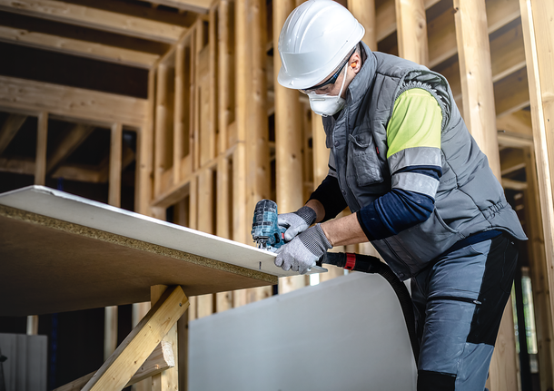 Person wearing safety equipment uses a power tool to cut a wooden board.