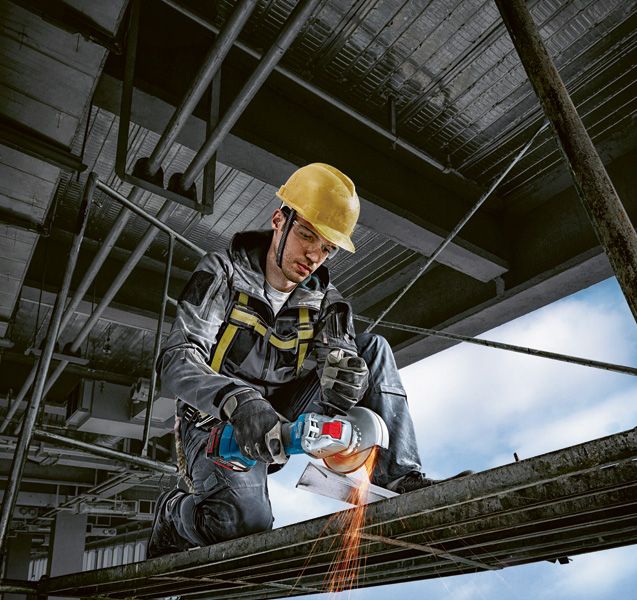 A person wearing safety equipment uses an angle grinder to cut metal beams.