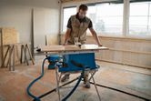 A person wearing safety equipment operates a cordless table saw cutting wood.