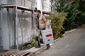 A worker wearing safety equipment carries a cordless table saw at a construction site.