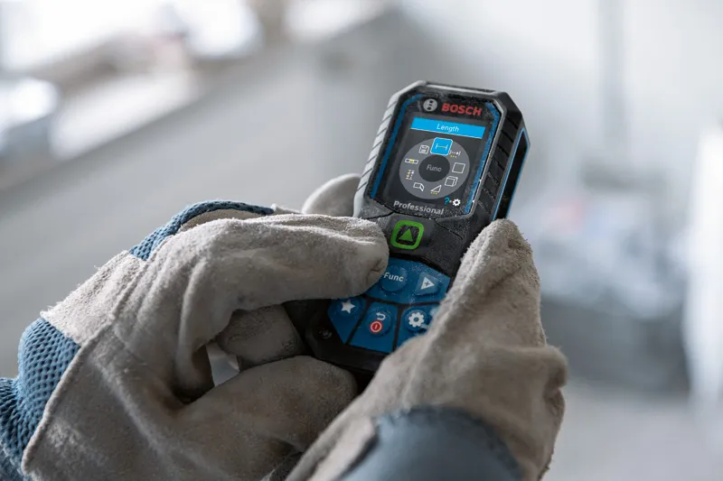 GLM 50-23 G Person wearing safety equipment operates a laser measure with a digital display.