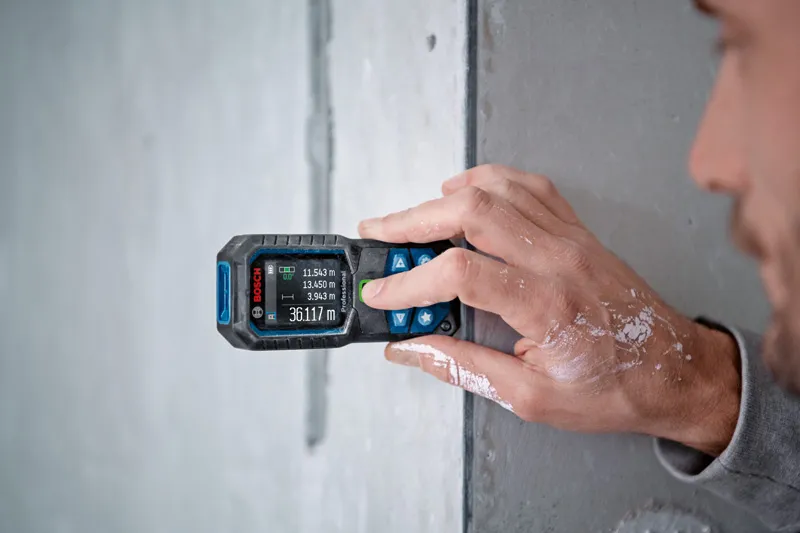GLM 50-23 G Person measuring wall distance with a laser measure, paint visible on their hand.