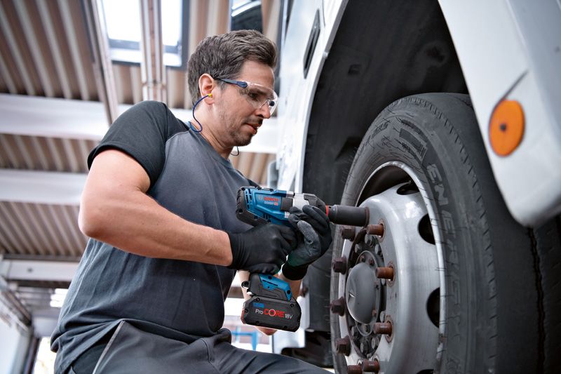 GDS 18V-1000 C A person wearing safety equipment uses an impact wrench on a truck wheel.