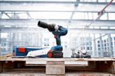 Cordless impact wrench on a wooden pallet beside bolts and a blue carrying case at construction site.