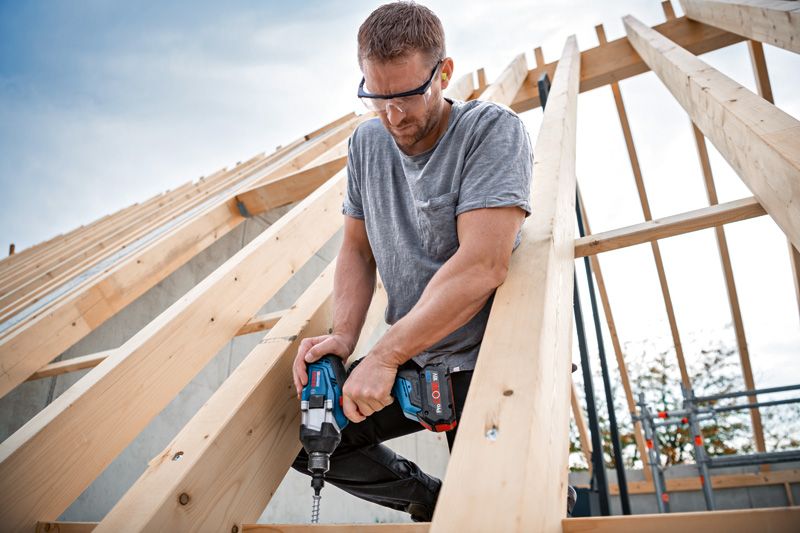 GDS 18V-1000 C A person wearing safety equipment fastens a screw into a wooden frame using an impact wrench.